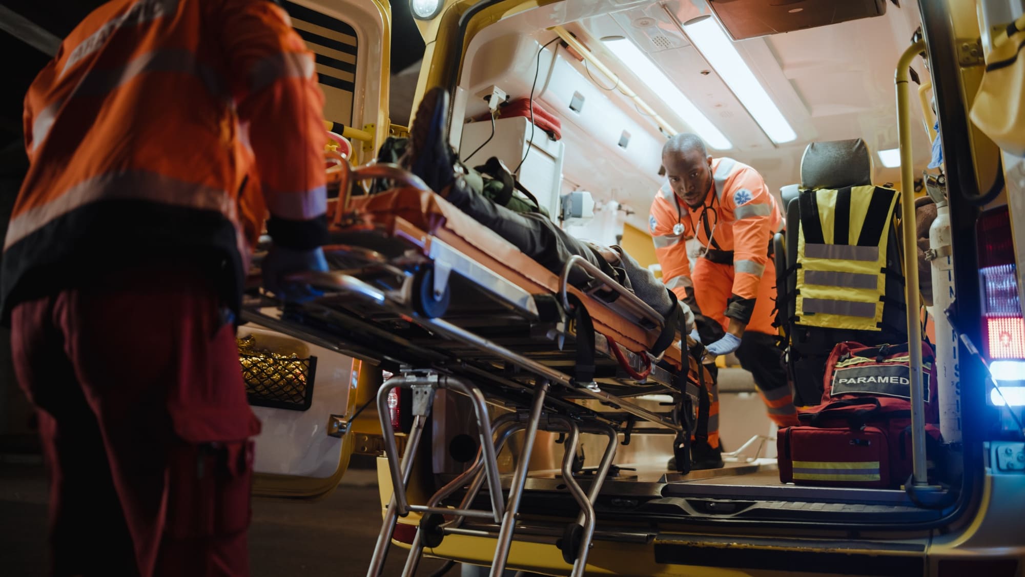 Paramedic in orange uniform loading patient on stretcher into ambulance at night